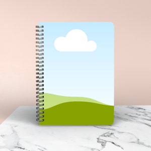 May include: A spiral bound notebook with a blue sky and green grass design. The cover features a white cloud.