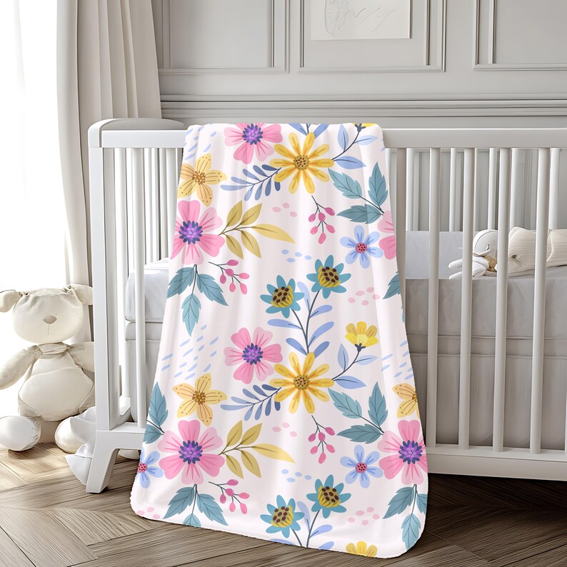 K&ouml;nnte beinhalten: Eine wei&szlig;e Babydecke mit einem Blumenmuster mit rosa, gelben, blauen und gr&uuml;nen Blumen. Die Decke ist weich und kuschelig, perfekt f&uuml;r ein Kinderzimmer.