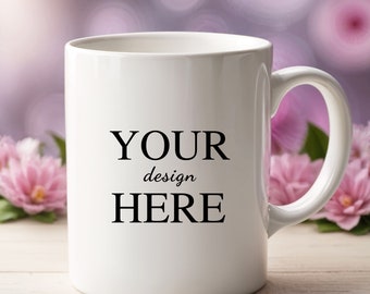 Könnte beinhalten: Eine weiße Keramiktasse mit einer schwarzen Aufschrift, die "YOUR design HERE" lautet. Die Tasse steht auf einer weißen Holzoberfläche mit rosa Blumen im Hintergrund.