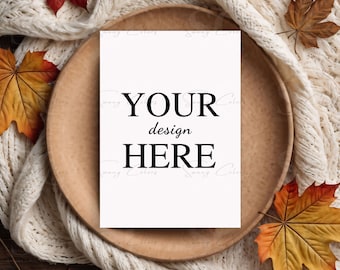 May include: A white card with the text "YOUR design HERE" on a wooden plate surrounded by a white knitted blanket and autumn leaves.