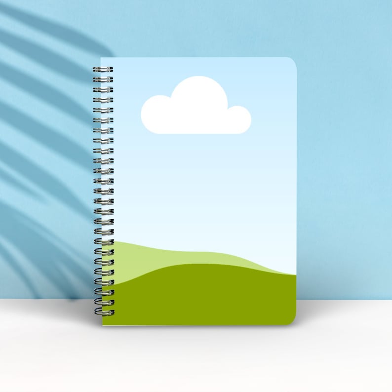 May include: A spiral bound notebook with a blue cover featuring a white cloud and a green grassy hill.
