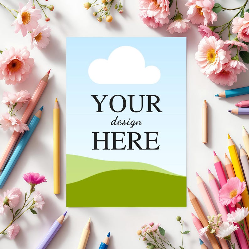 May include: A rectangular card featuring a light blue sky with a white cloud and green rolling hills, with the black text "YOUR design HERE" centred. The card is surrounded by various coloured pencils and pink flowers on a white surface.