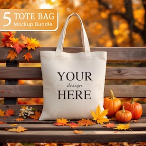 May include: A cream-colored tote bag with the text "YOUR design HERE" is displayed on a wooden bench. The scene is decorated with orange pumpkins and autumn leaves. The image also includes the text "5 TOTE BAG Mockup Bundle".