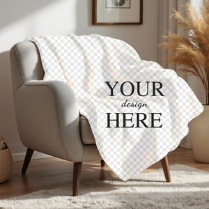 Może przedstawiać: Biały koc położony na jasnoszarym fotelu z drewnianymi nogami. Na kocu widnieje napis "YOUR design HERE".