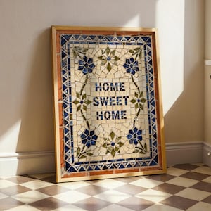 May include: A framed mosaic artwork with the words "HOME SWEET HOME" in blue lettering. The mosaic features a floral design with blue and green accents, set against a cream-colored background. The frame is a warm, natural wood tone.