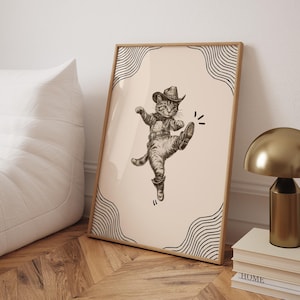 May include: A framed print of a cartoon cat wearing a cowboy hat and boots, kicking its leg up in the air. The cat is drawn in black and white on a light pink background with black and white wavy lines around the border.