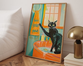 Può includere: Un gatto nero con gli occhi gialli si trova in un lavandino da bagno con piastrelle arancioni e blu. Il gatto sta alzando la zampa verso un asciugamano che dice "Lava le tue zampe".