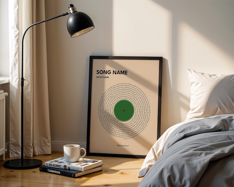 May include: A framed print with a circular design resembling a vinyl record. The print features a green center and text arranged in concentric circles. The words "SONG NAME" and "ARTIST NAME" are at the top. A black floor lamp and a white mug are also visible.