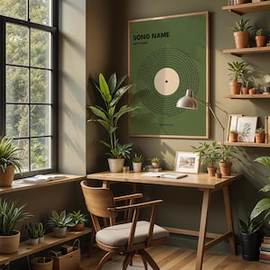 May include: A cozy home office with a wooden desk, chair, and shelves filled with plants and books. A framed green poster with the text "SONG NAME" and a vinyl record design hangs on the wall. A window with a view of greenery is on the left.