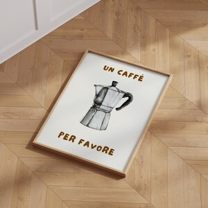 May include: A framed print with a white background and brown text that reads "Un Caffe Per Favore". A black and white illustration of a traditional Italian coffee pot is in the center of the print.