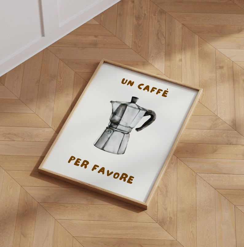 May include: A framed print with a white background and brown text that reads "Un Caffe Per Favore". A black and white illustration of a traditional Italian coffee pot is in the center of the print.