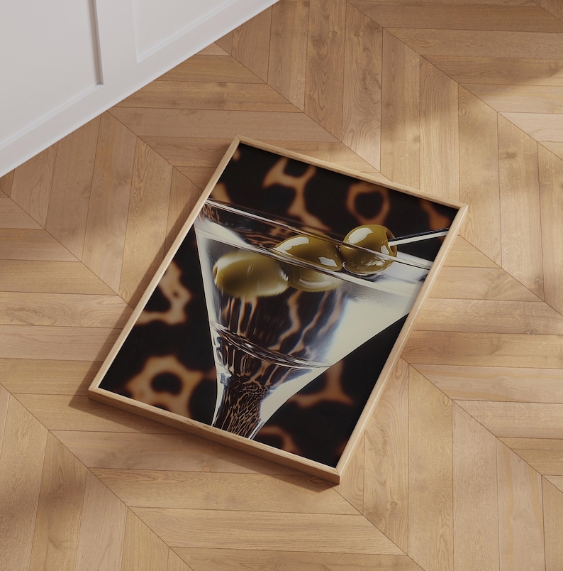 May include: A close-up of a martini glass filled with a clear liquid and three green olives. The glass is on a black and brown patterned background.