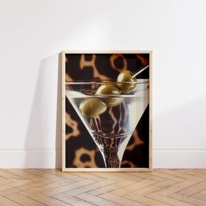 May include: A framed print of a martini glass with green olives, set against a brown and black animal print background.