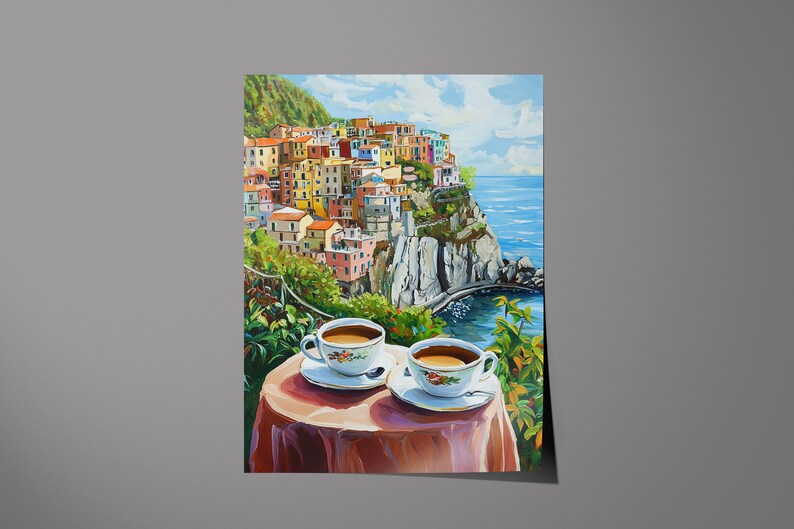 May include: Two cups of coffee on a table with a red tablecloth, overlooking a colorful Italian village built on a cliffside with a blue ocean in the background.