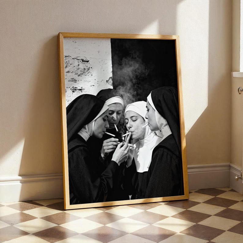 May include: Black and white framed print featuring four nuns in traditional habits, smoking cigarettes. One nun lights a cigarette for another, with smoke rising. The image is set against a neutral background.