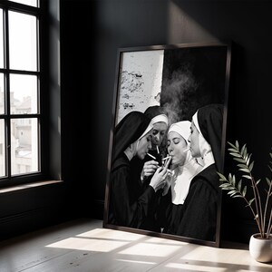 May include: Black and white framed print featuring a group of nuns smoking cigarettes. The image shows the nuns in their traditional habits, with smoke rising from the lit cigarettes. The artwork is displayed in a dark room with a window.