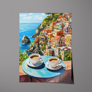 May include: Two white coffee cups with brown coffee on a blue table with a view of a colorful Italian village on a cliff overlooking the ocean.