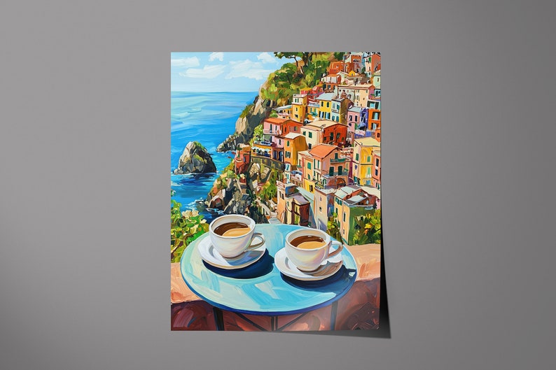 May include: Two white coffee cups with brown coffee on a blue table with a view of a colorful Italian village on a cliff overlooking the ocean.