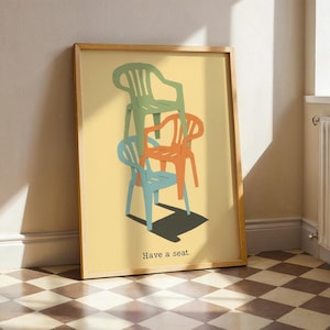 May include: A framed art print featuring a stack of three colorful plastic chairs in green, orange, and blue against a yellow background. The text "Have a seat" is at the bottom. The artwork is in a wooden frame.