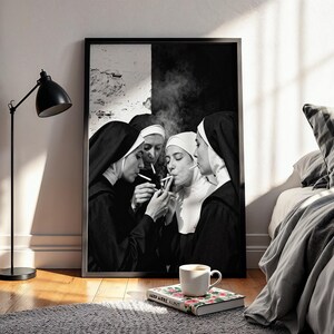 May include: Black and white framed print featuring four nuns in traditional habits, smoking cigarettes. The image is set against a black and white backdrop, with smoke rising. A coffee cup and a book are in the foreground, resting on a gray rug.