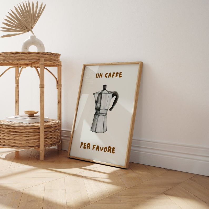 May include: A framed print with a white background and brown text that reads "Un Caffe Per Favore". The print features a black and white illustration of a traditional Italian coffee pot.