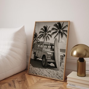 May include: Black and white framed print of a vintage SUV parked on a sandy beach with a surfboard leaning against it. Palm trees are in the background, evoking a tropical, coastal theme.