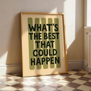 May include: A framed print featuring the phrase "WHAT'S THE BEST THAT COULD HAPPEN" in black text. The background is light beige with vertical green brushstrokes. The frame is a light wood colour.