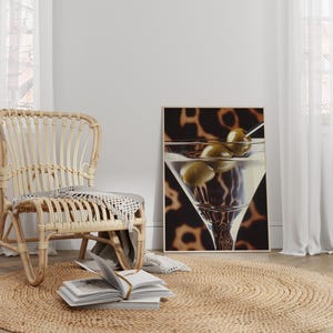 May include: A wicker chair with a woven seat and back sits on a jute rug in front of a white wall. A framed print of a martini glass with olives hangs on the wall.