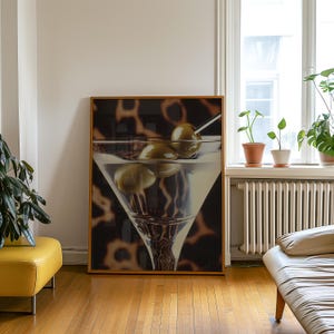 May include: A framed print of a martini glass with three green olives. The background is a blurred image of a leopard print.