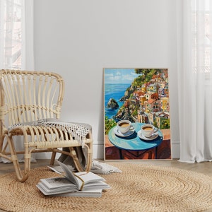 May include: A painting of a colorful Italian village on a cliff overlooking the ocean. Two white coffee cups sit on a blue table in the foreground.