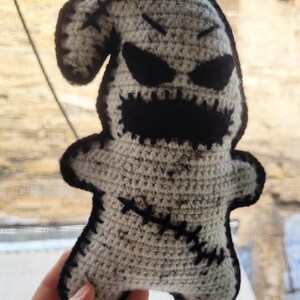 May include: Crocheted ghost plush toy with black eyes, a stitched mouth, and black stitching details. The ghost is white with a speckled texture.