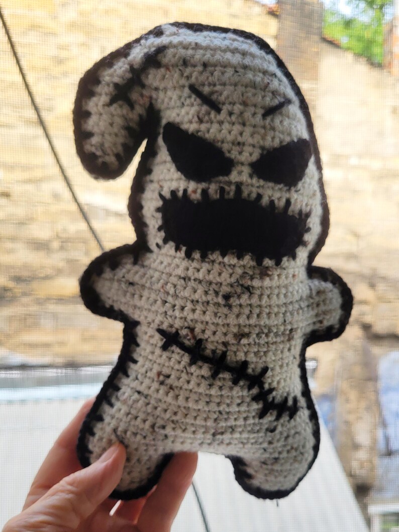 May include: Crocheted ghost plush toy with black eyes, a stitched mouth, and black stitching details. The ghost is white with a speckled texture.