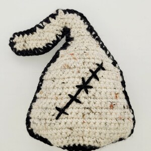 May include: A white crocheted stuffed toy shaped like a sack with a black crocheted border and a black stitched X across the front.