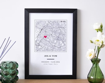 May include: A black framed print with a map of Paris, France. A red heart is placed on the map. The text below the map reads "AVA & TOM ENGAGED - 14.02.2024 Eiffel Tower, Paris".
