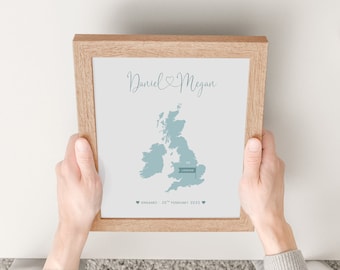 May include: A framed print with a light blue map of the United Kingdom. The map shows the location of London. The text "Daniel & Megan" is at the top of the print. The text "Engaged - 25th February 2021" is at the bottom of the print.