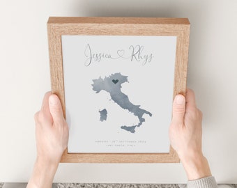 May include: A framed print with a watercolor map of Italy. The map is in shades of blue and gray, with a small heart marking a location. The print also includes the names "Jessica & Rhys" and the text "Married: 18th September 2023, Lake Garda, Italy."