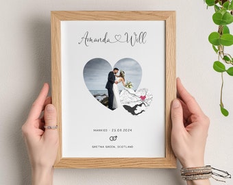 May include: A framed print featuring a wedding photo within a heart-shaped cutout. The print includes the names "Amanda & Will", the wedding date "23.08.2024", and a map with a heart marking the location. The frame is made of light-colored wood.