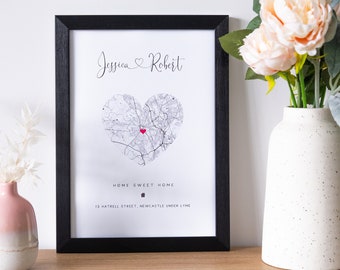 May include: A black framed print with a white background. The print features a heart-shaped map with a red dot in the center. The text "Jessica ♥ Robert" is at the top of the print. The text "Home Sweet Home" is below the map, along with the address "15 Hattrell Street, Newcastle Under Lyme."