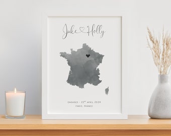 May include: A white framed print with a watercolor map of France. The map is in shades of gray with a black heart marking Paris. The text "Jake & Holly" is at the top of the print, and the text "ENGAGED - 22nd April 2024 PARIS, FRANCE" is at the bottom.
