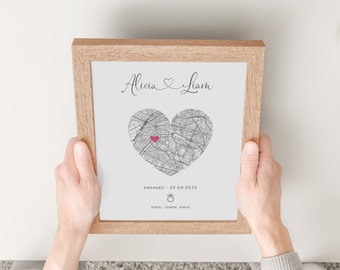 May include: A framed print in a light wood frame featuring the names Alicia and Liam with a heart-shaped map of Paris. A small pink heart marks a location on the map. Below the map, the text reads ENGAGED - 22.04.2022 with a ring icon and EIFFEL TOWER, PARIS.