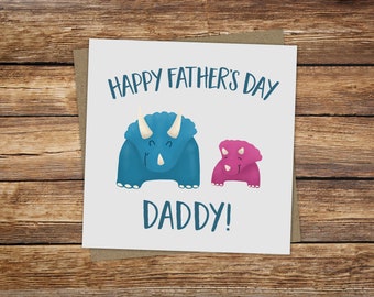 May include: A white card with the text "Happy Father's Day Daddy!" in blue and pink. Two cartoon dinosaurs, one blue and one pink, are on the card.
