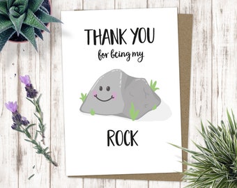 May include: A white card with the text "THANK YOU for being my ROCK" in black. A cartoon gray rock with a smiling face is in the center of the card.