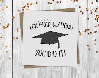 May include: A white card with a black graduation cap and the text "CON-GRAD-ULATIONS! YOU DID IT!" printed on it. The card is surrounded by gold glitter stars.