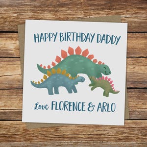May include: A square greeting card with a watercolor illustration of three dinosaurs. The card reads "HAPPY BIRTHDAY DADDY" above the dinosaurs and "Love FLORENCE & ARLO" below. The card is on a brown envelope.