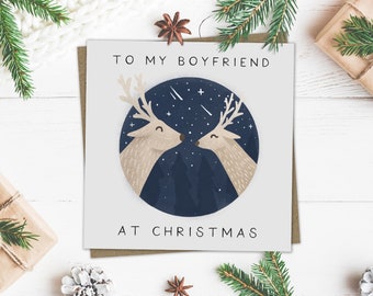 May include: A Christmas card with the text "TO MY BOYFRIEND AT CHRISTMAS". The card features a circular illustration of two deer kissing under a starry night sky. The deer are light brown with white antlers, set against a dark blue background.