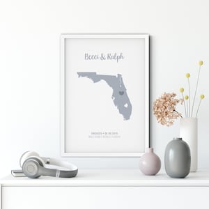 Puede incluir: Una impresión enmarcada en blanco con un mapa gris de Florida. El mapa tiene un corazón que marca la ubicación de Walt Disney World. El texto "Becci & Ralph" está en la parte superior de la impresión. El texto "ENGAGED - 08.09.2019 WALT DISNEY WORLD, FLORIDA" está en la parte inferior de la impresión.