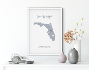 May include: A white framed print with a gray map of Florida. The map has a heart marking the location of Walt Disney World. The text "Becci & Ralph" is at the top of the print. The text "ENGAGED - 08.09.2019 WALT DISNEY WORLD, FLORIDA" is at the bottom of the print.
