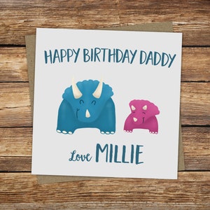 Puede incluir: Una tarjeta blanca con una ilustraci&oacute;n de dinosaurio azul y rosa. La tarjeta dice "Feliz cumplea&ntilde;os pap&aacute;" y "Con amor Millie".