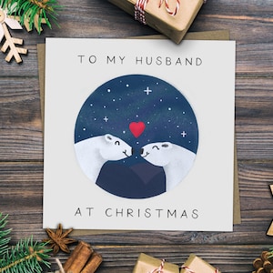 Puede incluir: Una tarjeta blanca con el texto "To my husband at Christmas" y una ilustración circular de dos osos polares besándose bajo un cielo estrellado con un corazón rojo.