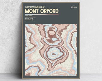 May include: A framed topographic map print of Mont Orford, Quebec, featuring a dark gray header with white text and a central graphic of layered contour lines in shades of cream, light blue, and muted brown, labeled with altitude 853 M.